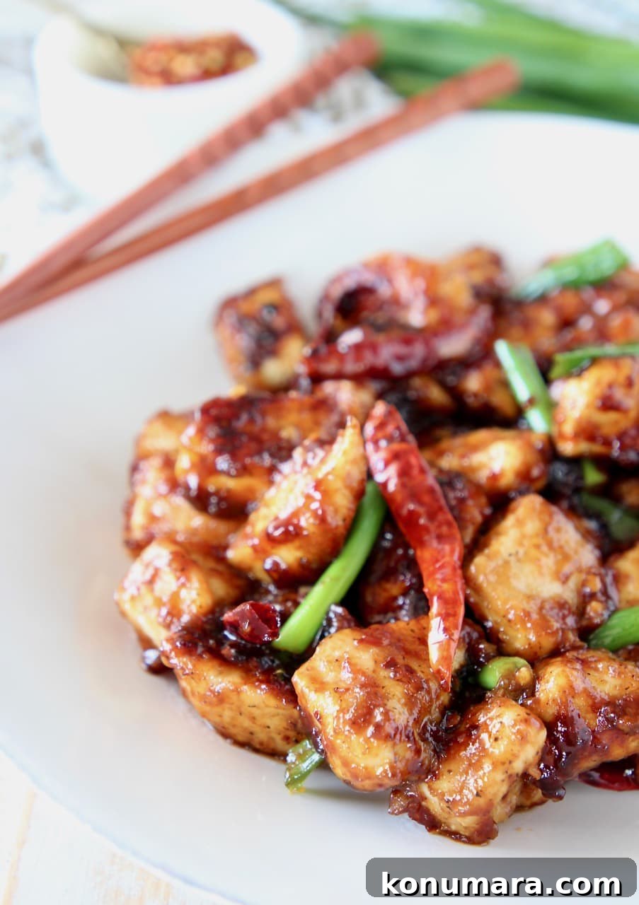 Gluten-Free General Tso's Chicken Recipe 2 Gluten free general tso chicken with red chili peppers and green onions on white plate with wood chopsticks