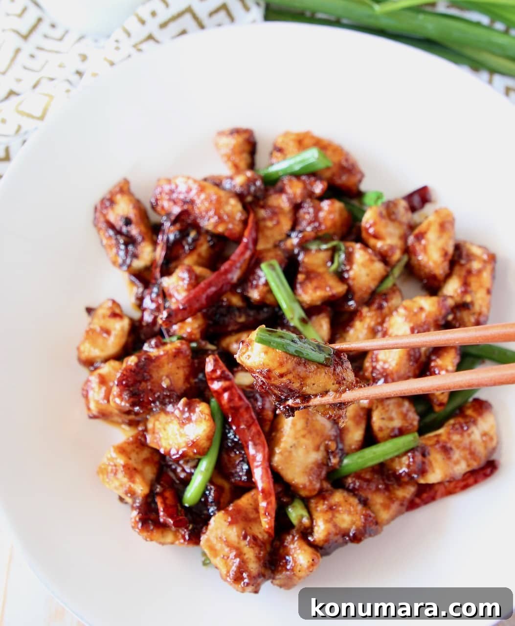 Gluten-Free General Tso's Chicken Recipe 3 General tso chicken on a white plate with chopsticks picking up a piece of chicken