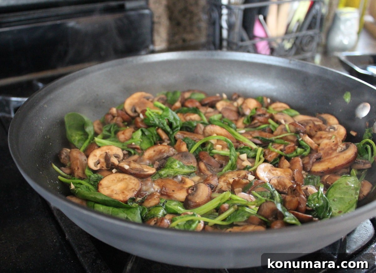 sliced mushrooms and fresh spinach leaves in a skillet on the stove