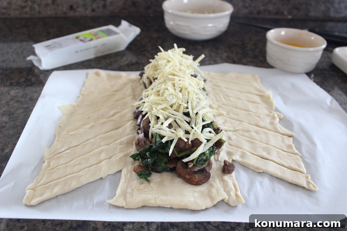 shredded cheddar cheese on top of spinach and mushrooms on sheet of puff pastry dough
