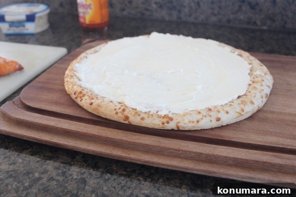 Buffalo Chicken Dip Pizza Recipe 5 A cooked pizza crust covered with a cheese sauce on a wooden cutting board.