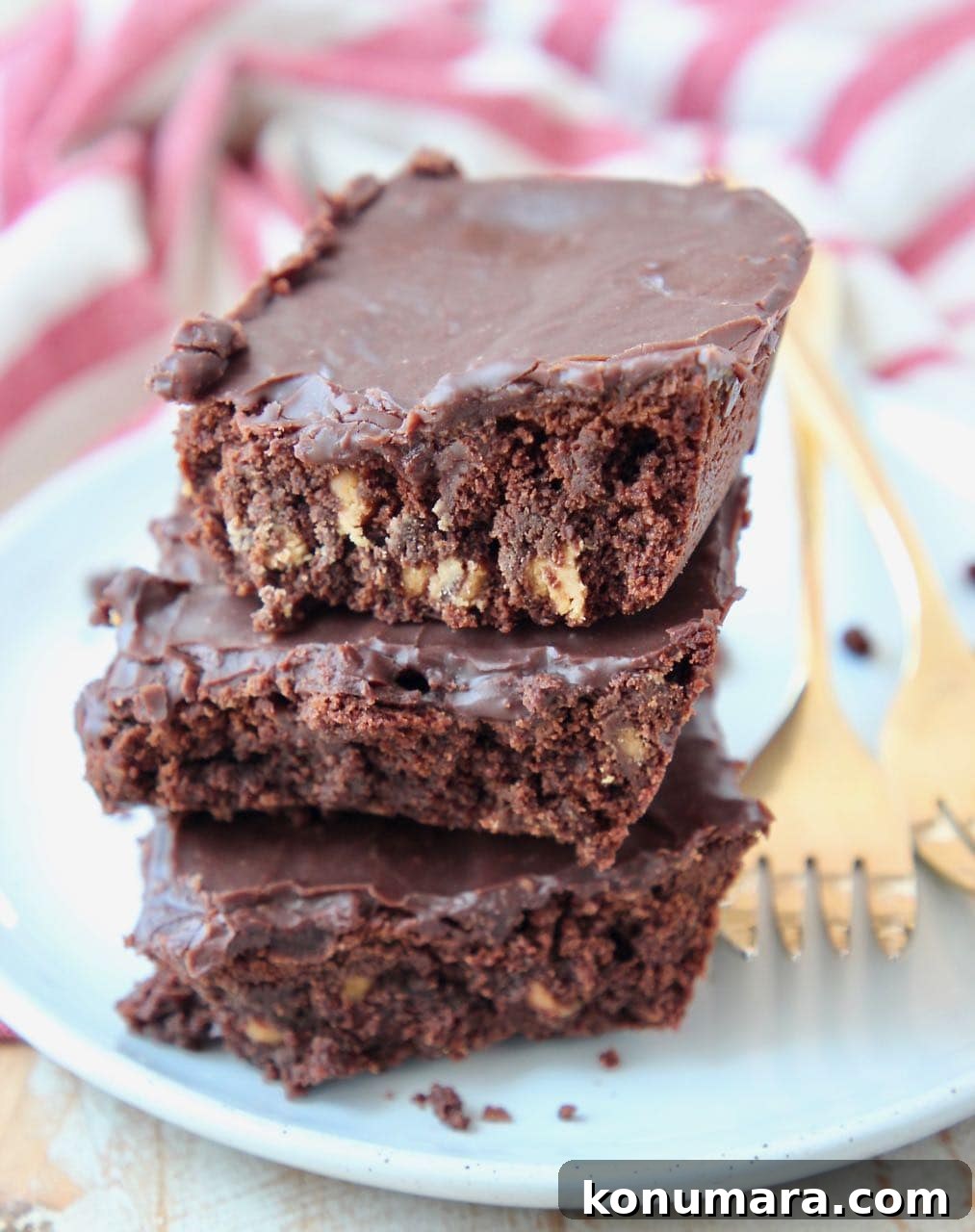 Three stacked brownies on a white plate with gold forks on the side