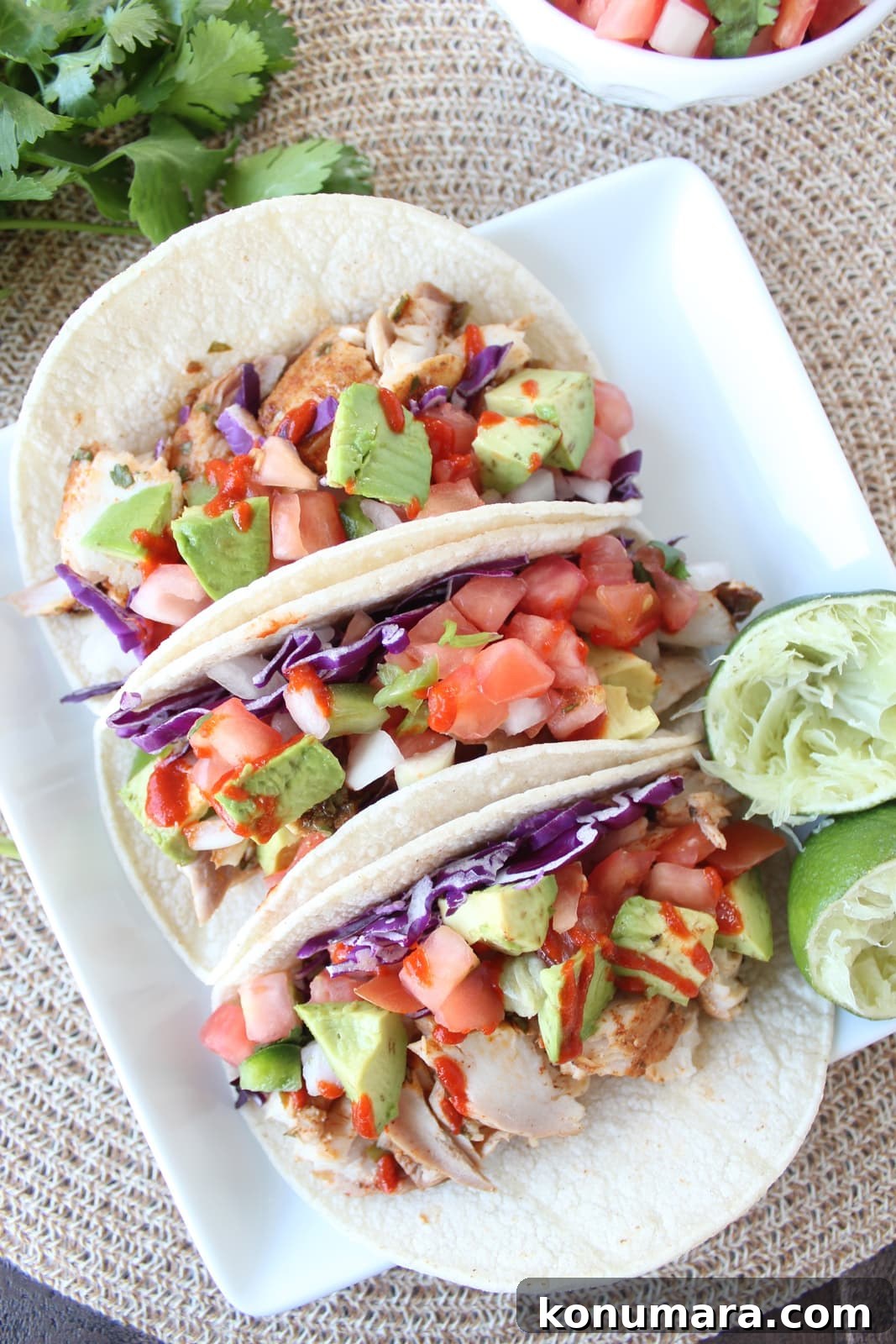 Grilled Mahi-Mahi Tacos with Avocado Lime Slaw 2 fish tacos on white plate, topped with diced avocado and hot sauce