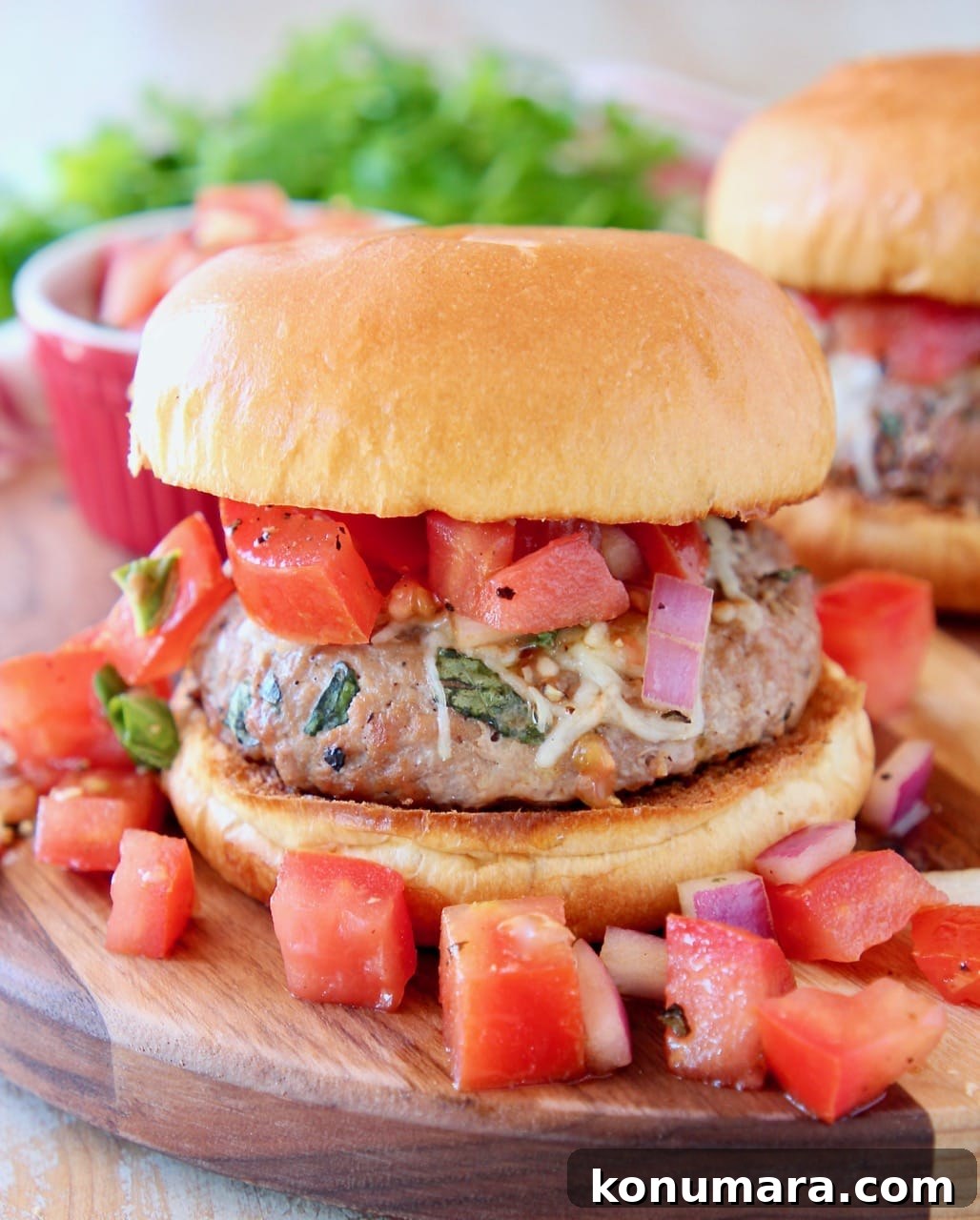Bruschetta Turkey Burgers with Tomato and Basil 2 Turkey burger on bun on wood cutting board topped with diced tomato bruschetta