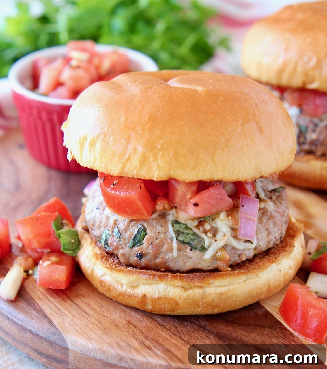 Bruschetta Turkey Burgers with Tomato and Basil 3 Turkey burger on bun topped with diced tomatoes and onions on wood cutting board