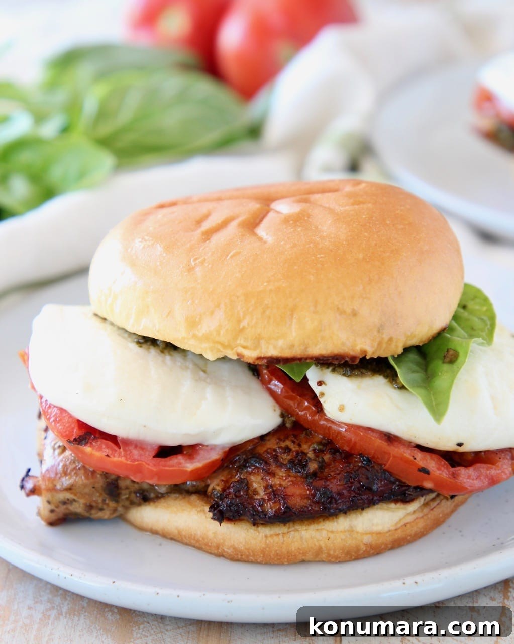Grilled Chicken Caprese Sandwich with Fresh Mozzarella and Basil 2 Grilled chicken sandwich with tomatoes and mozzarella cheese on white plate