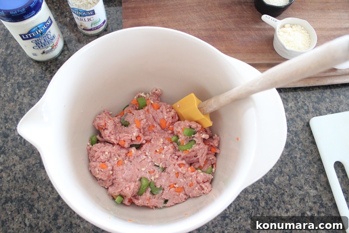 ground turkey and celery and carrots being mixed by a spatula in a white bowl 