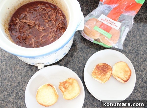 Slow-Cooked BBQ Brisket Sandwich with Smoky Sauce 9 shredded brisket in sauce in a crock pot next to two plates with toasted hamburger buns