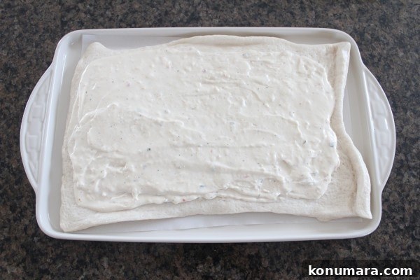white sauce spread on a rectangular pizza crust on a baking sheet