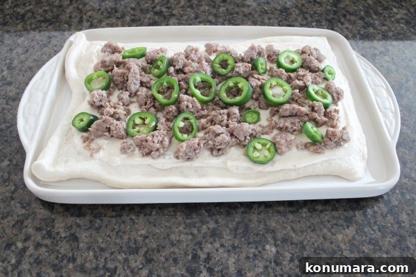 crumbled cooked sausage and sliced jalapenos on pizza dough on a baking sheet