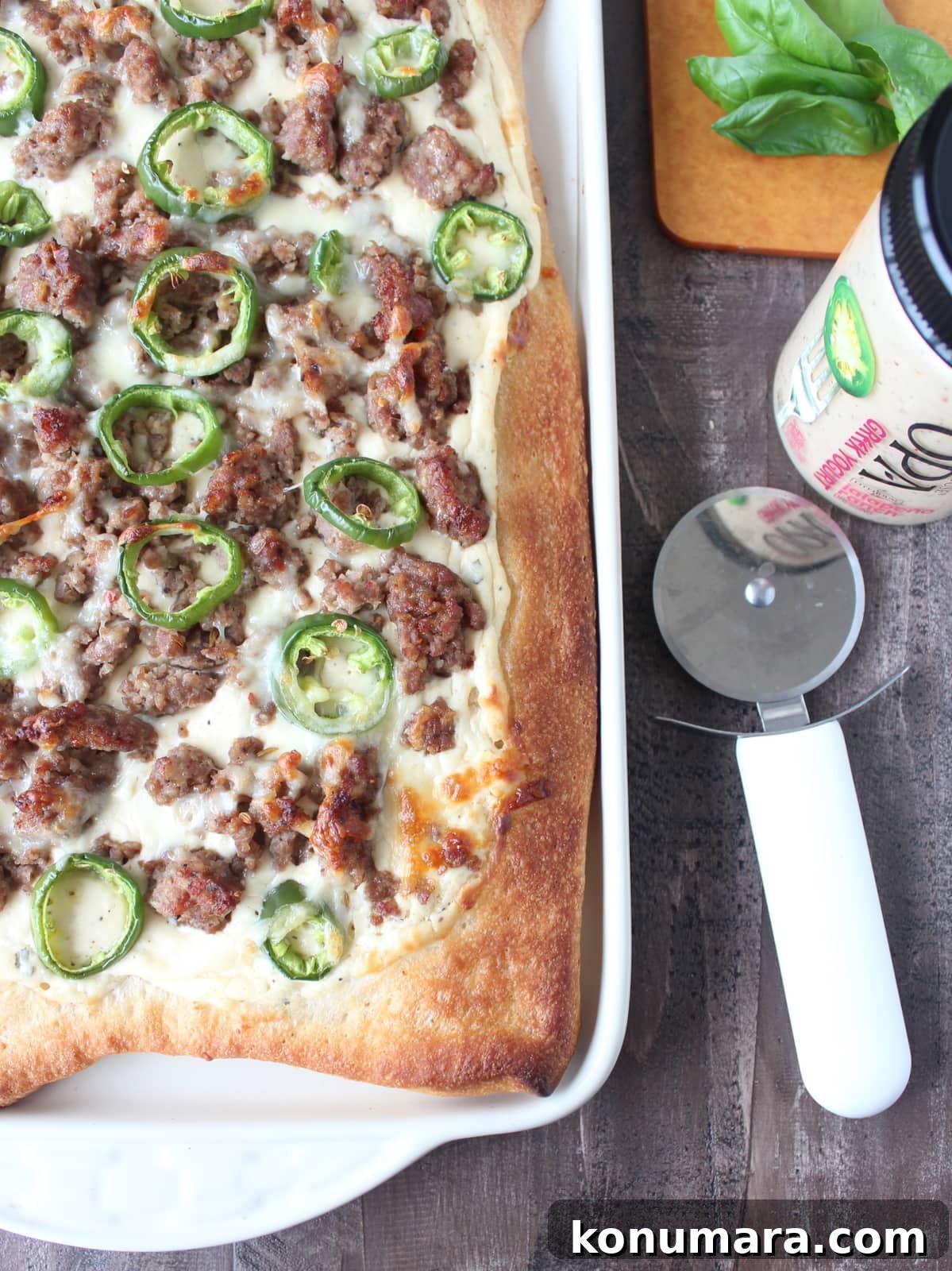 pizza on a baking sheet topped with crumbled sausage and sliced jalapenos