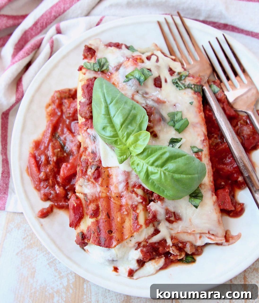 Three-Cheese Manicotti with Italian Sausage Marinara 5 Manicotti on plate with fresh basil leaves and copper forks