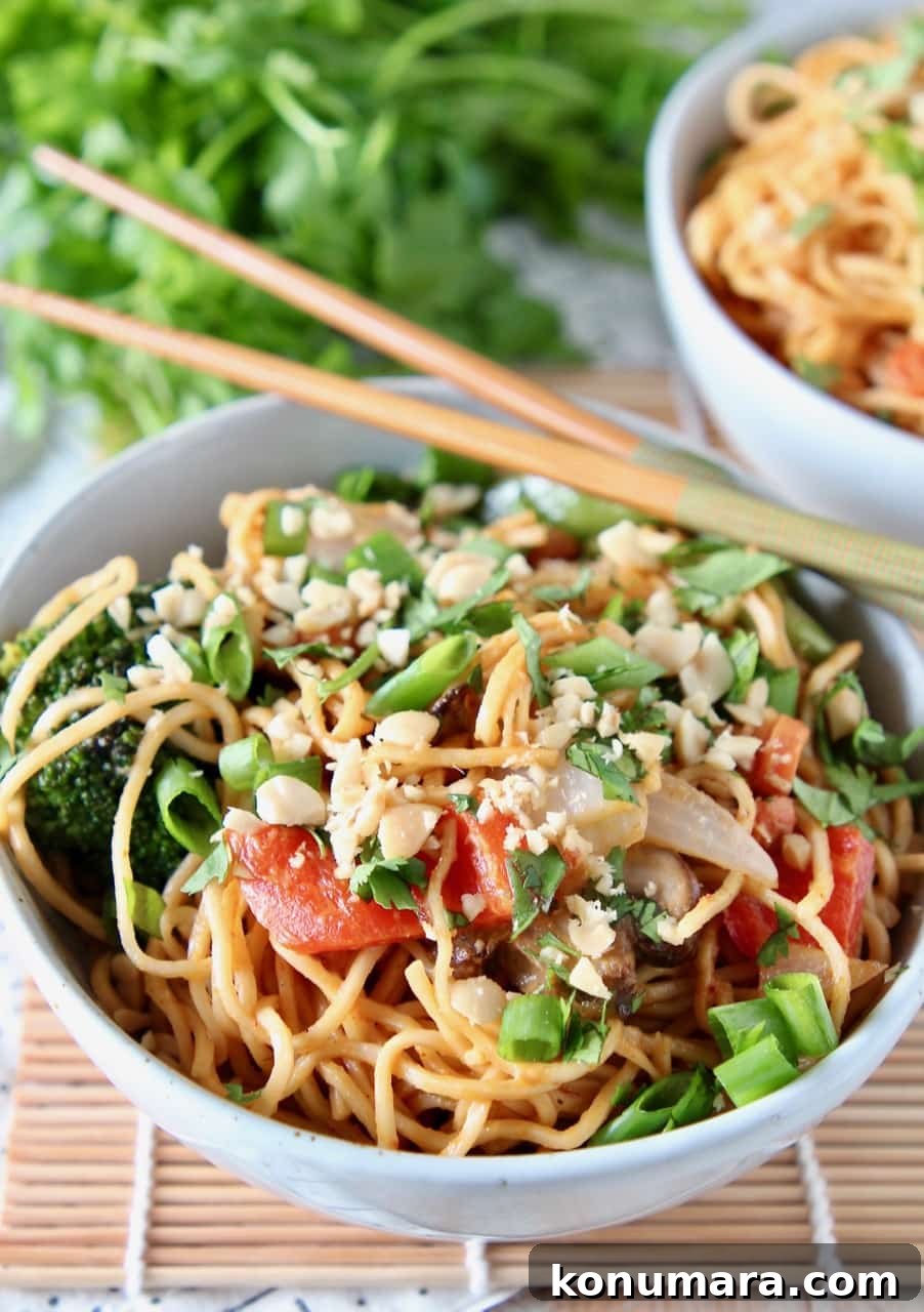 Ramen noodles and vegetables tossed with Thai peanut sauce in bowl with chopsticks on the side