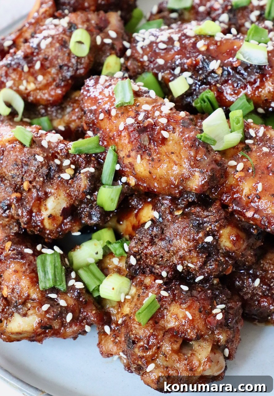 cooked chicken wings tossed in sauce piled up on a plate, topped with diced green onions and sesame seeds