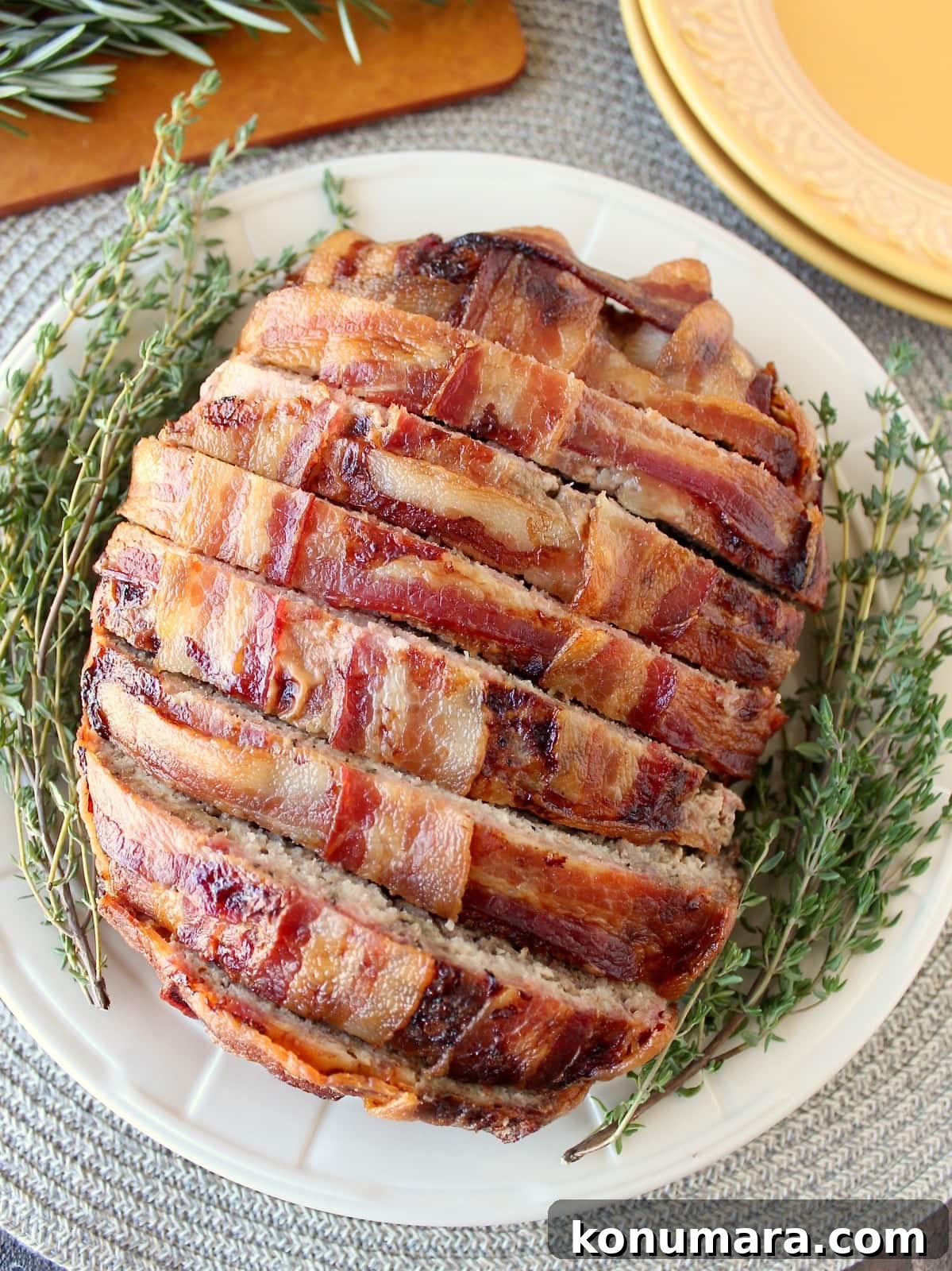 Juicy Bacon-Wrapped Meatloaf Recipe 2 Sliced bacon wrapped meatloaf on plate with fresh herbs