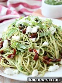 Pesto spaghetti on plate with goat cheese crumbles on top and gold fork on the side