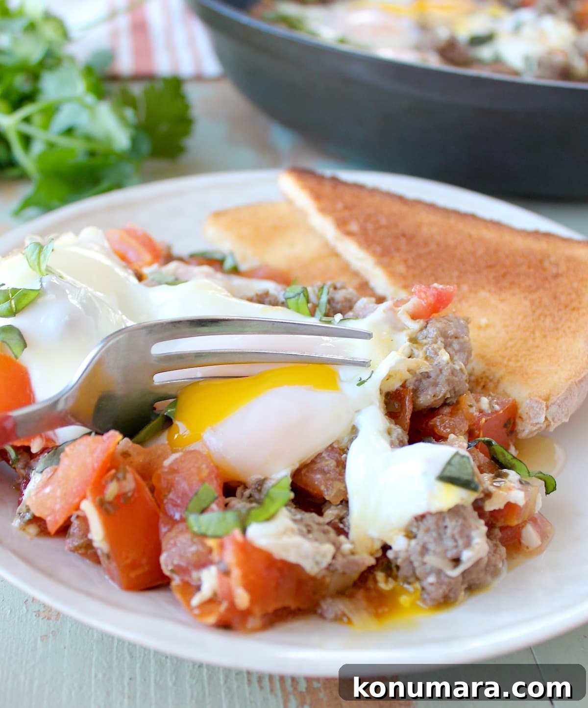 fork in a yolky egg on top of diced tomatoes tossed with cooked turkey sausage with toast on the side