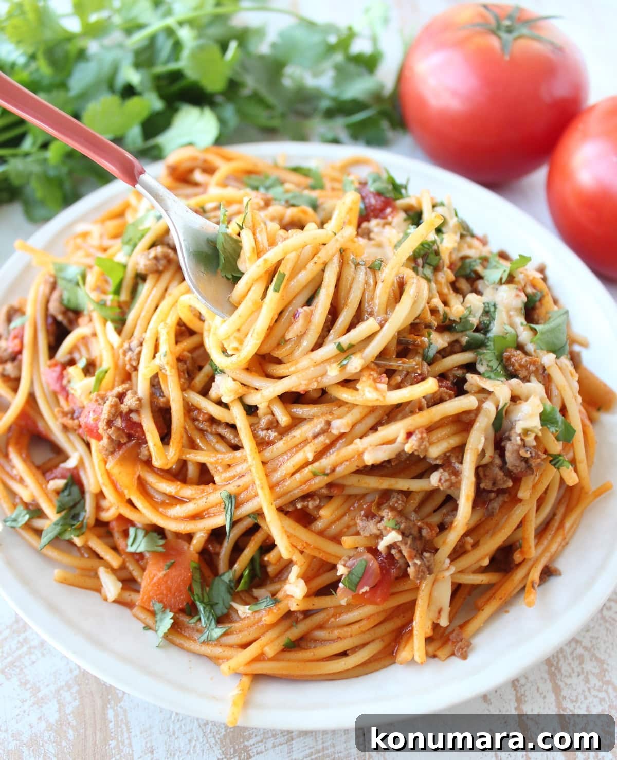 A fork scooping up a bite of One Pot Buffalo Taco Spaghetti on a white plate.