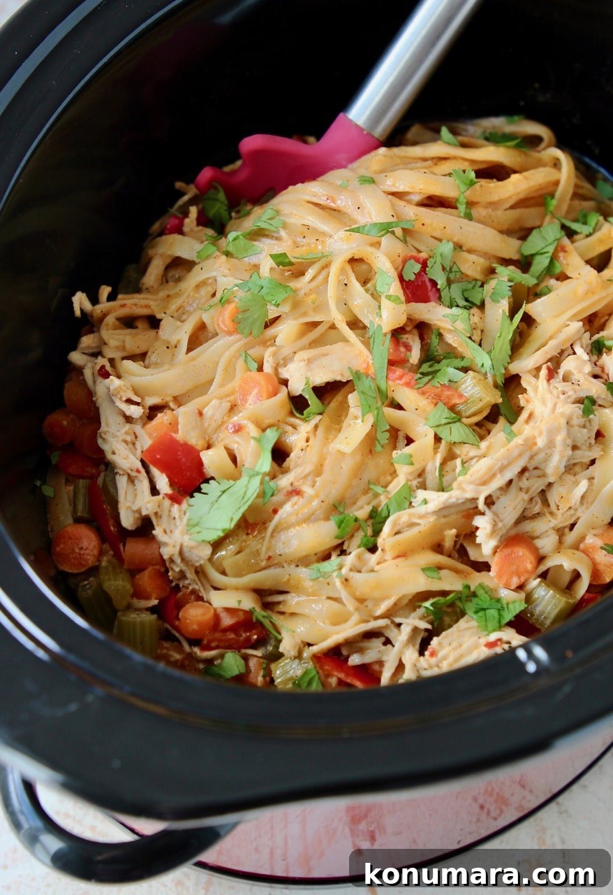 Slow Cooker Buffalo Chicken Alfredo Recipe 4 Buffalo chicken alfredo in a crock pot with carrots and red bell peppers, topped with fresh cilantro leaves, with a red spoon in the crock pot