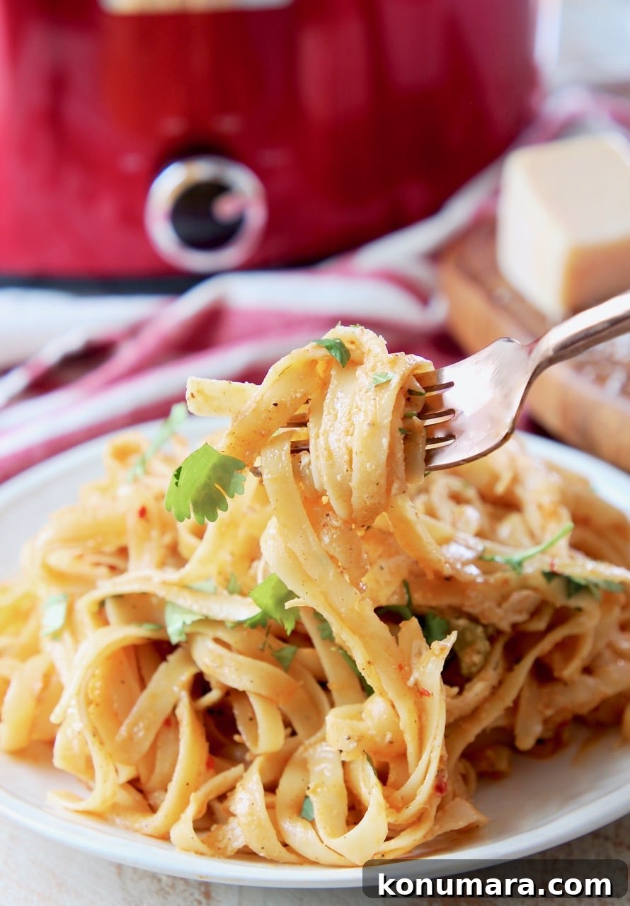 Slow Cooker Buffalo Chicken Alfredo Recipe 5 Crock pot chicken alfredo on plate, with a fork wrapped in noodles lifting off the plate and red crock pot in background