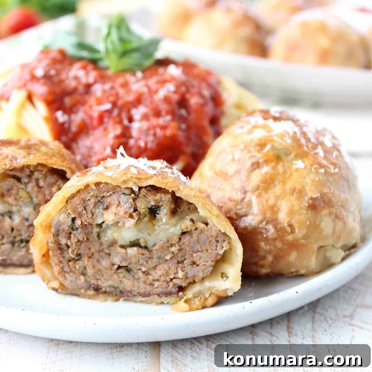 baked puff pastry wrapped meatball cut in half on plate with spaghetti and red sauce