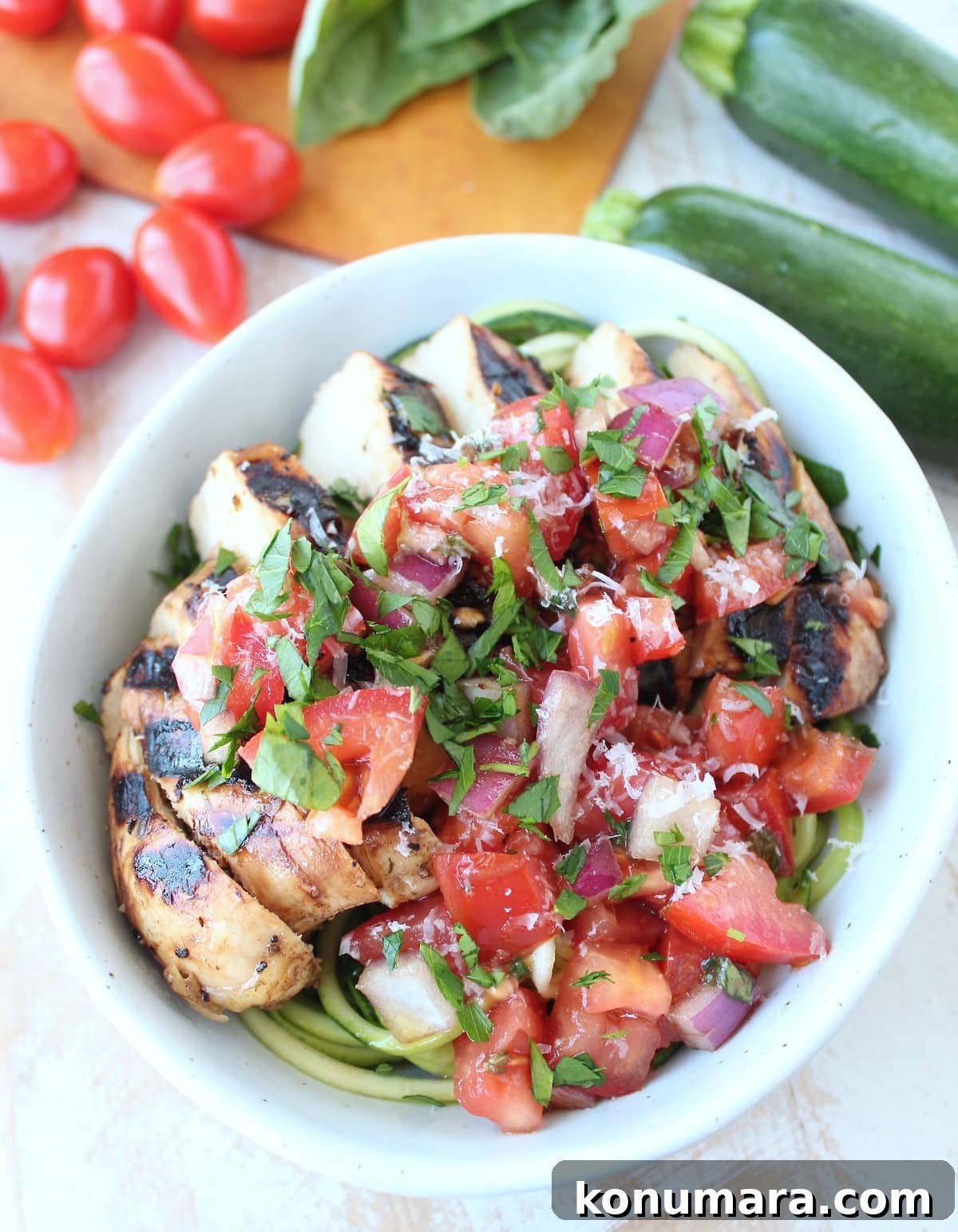 Tomato bruschetta on top of sliced grilled chicken breast in bowl with zucchini noodles