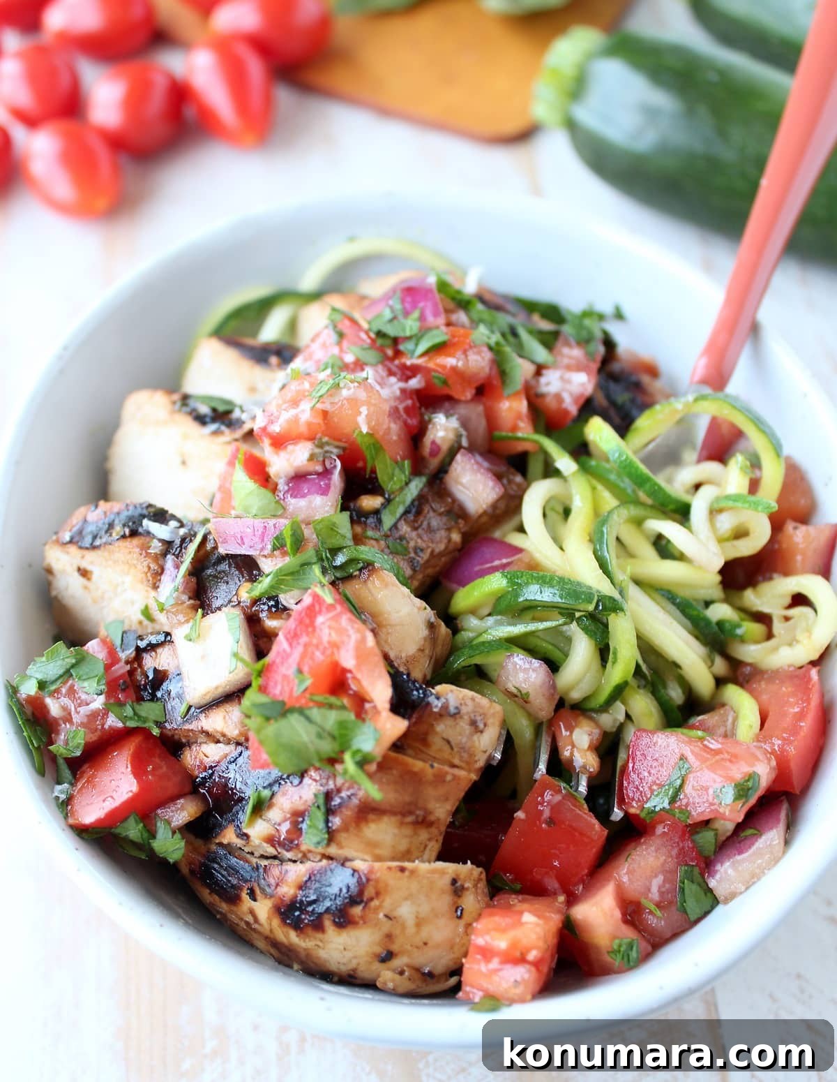 Zucchini noodles spun around a fork in a bowl with tomato basil bruschetta and grilled chicken