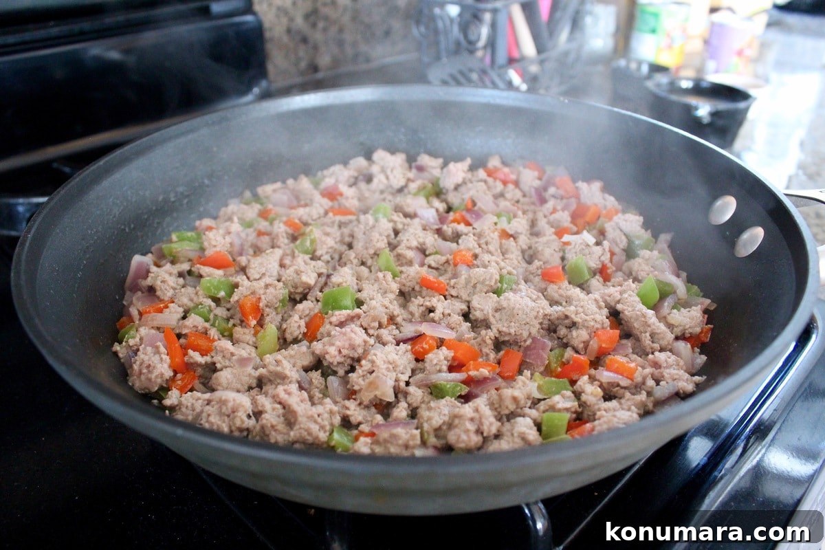 Ground turkey, onions, and bell peppers cooking in a skillet.