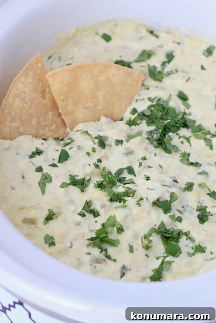 White queso dip in crock pot topped with fresh cilantro, with tortilla chips in the dip
