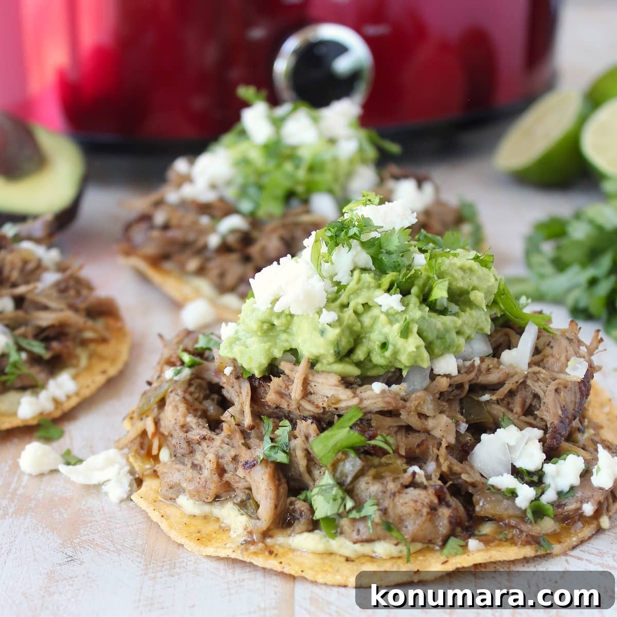 cooked carnitas on top of tostada shell topped with guacamole and cheese