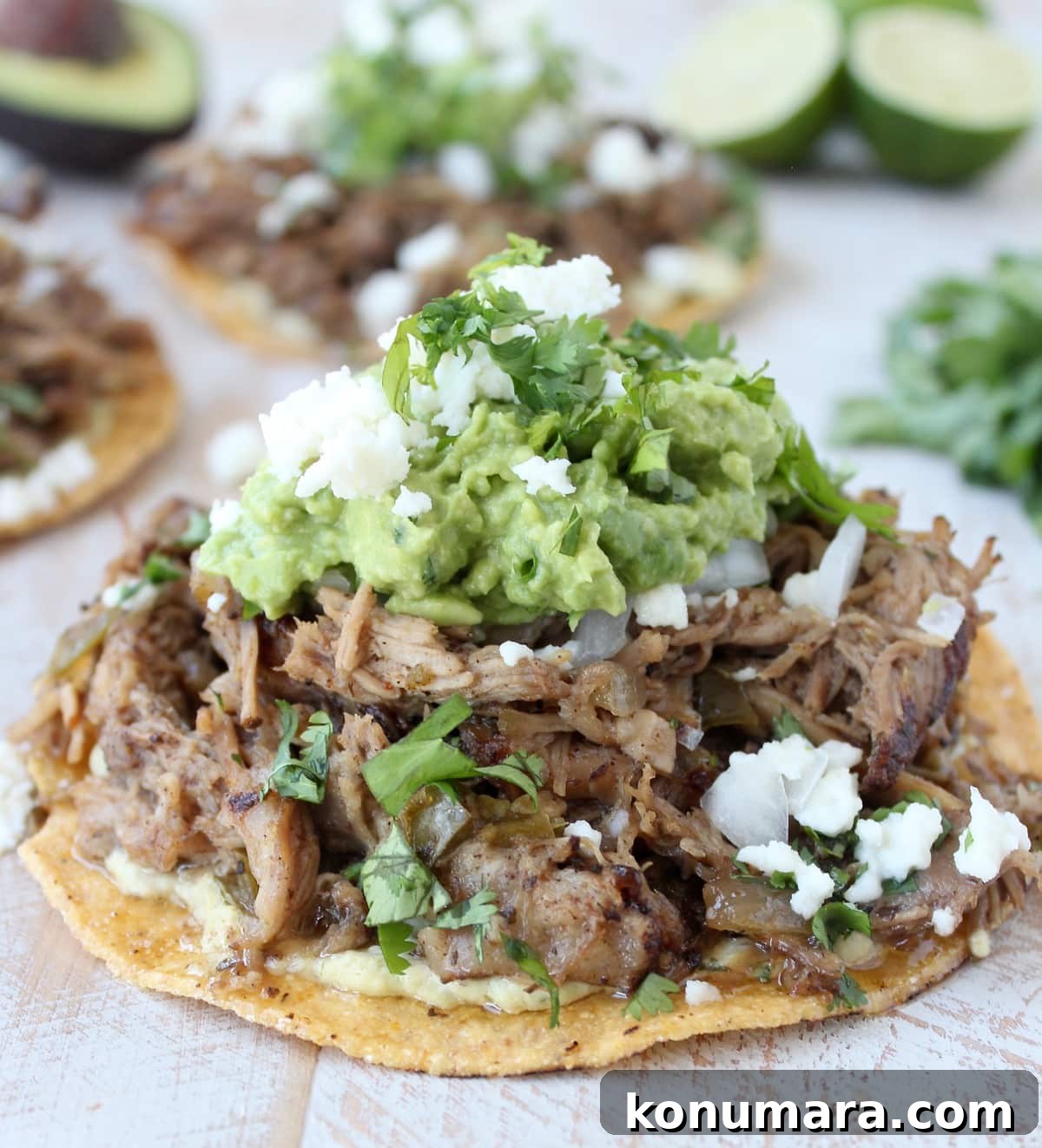 cooked, shredded pork on top of tostada with guacamole and crumbled cheese