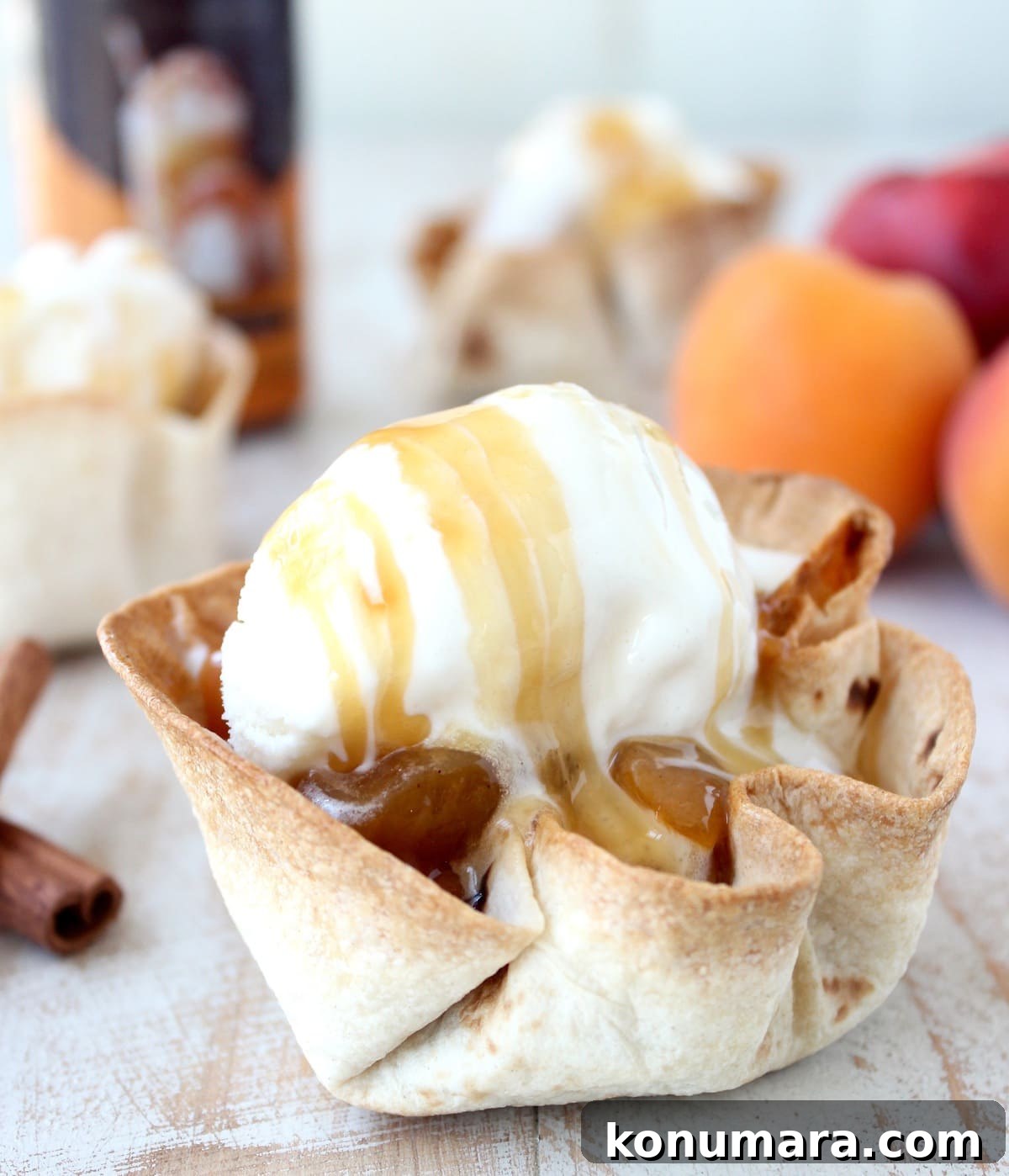 crispy taco shell cups filled with cooked fruit, topped with a scoop of ice cream and caramel syrup on a white wood board