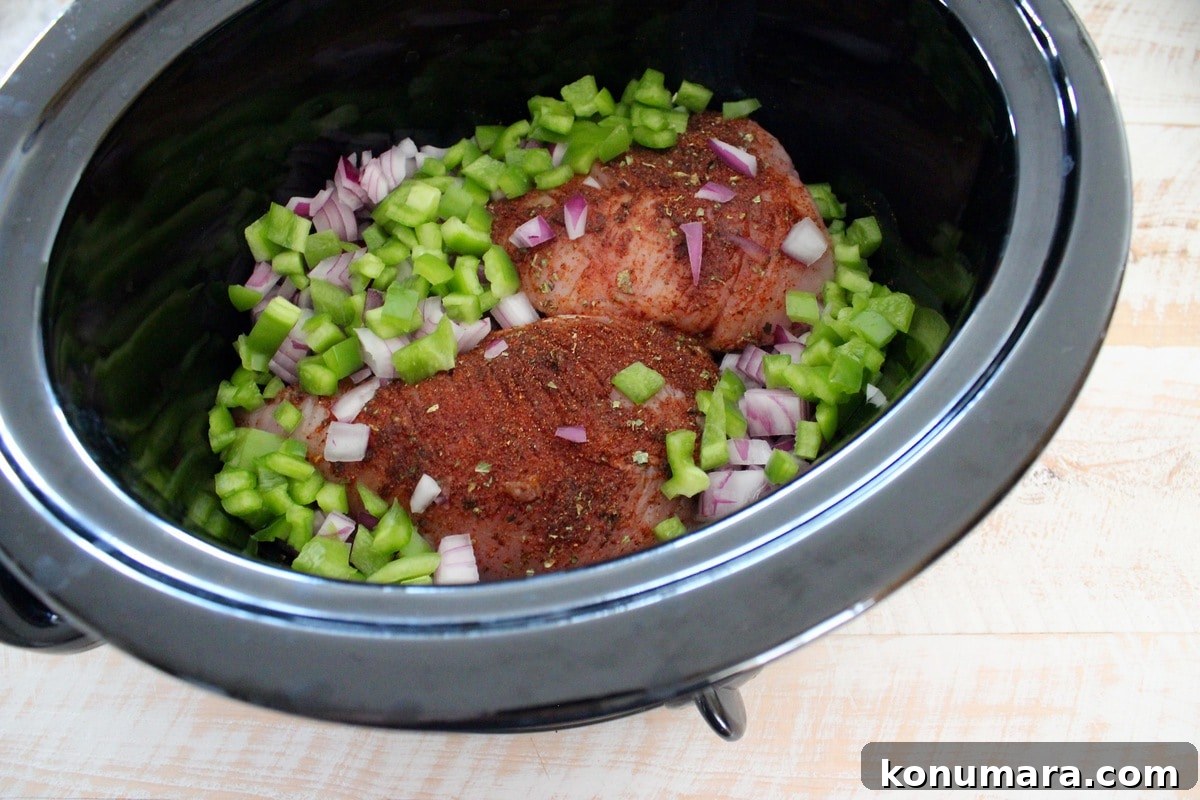 Slow Cooker Cheesy Turkey Taco Soup Recipe 4 A black crock pot bowl filled with seasoned chicken, diced peppers, and onions.