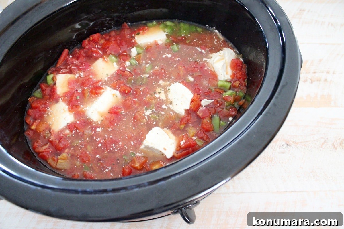 Slow Cooker Cheesy Turkey Taco Soup Recipe 5 A slow cooker filled with diced peppers, diced tomatoes, broth, and chunks of cream cheese.