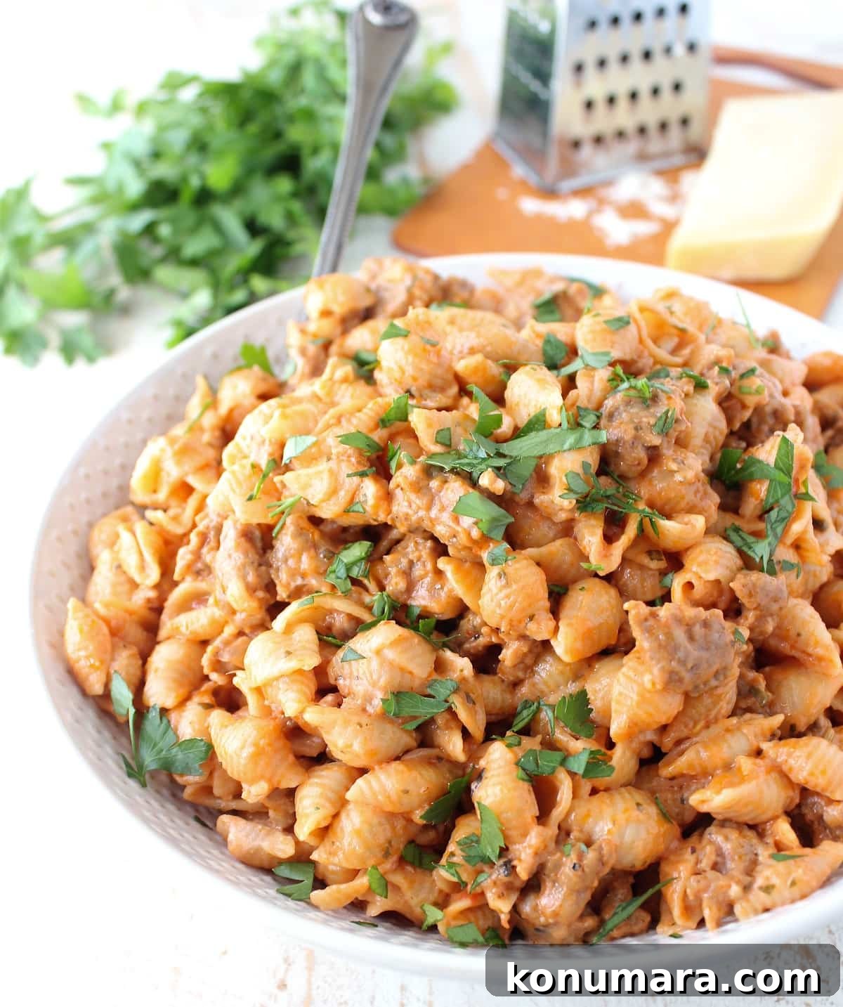 cooked pasta shells in a cheesy sauce with sausage in a bowl with a serving spoon topped with fresh chopped parsley