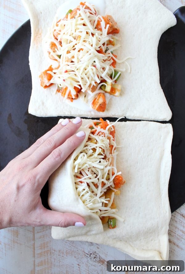 Cheesy Buffalo Chicken Bake Recipe 4 Hand folding uncooked pizza dough over chicken, celery, carrots, green onions, buffalo sauce and cheese.