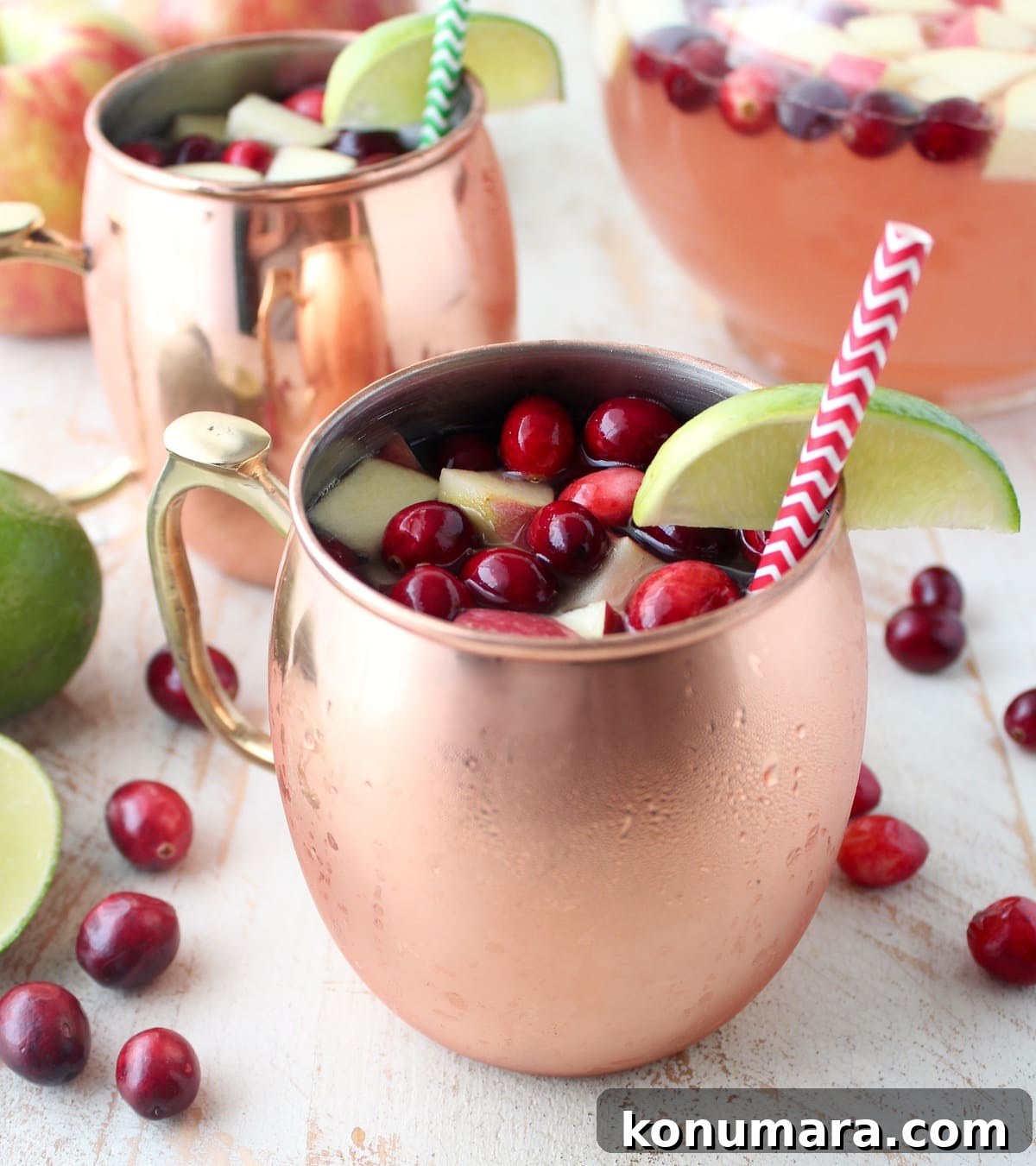 copper mugs filled with moscow mule punch with fresh cranberries and diced apples