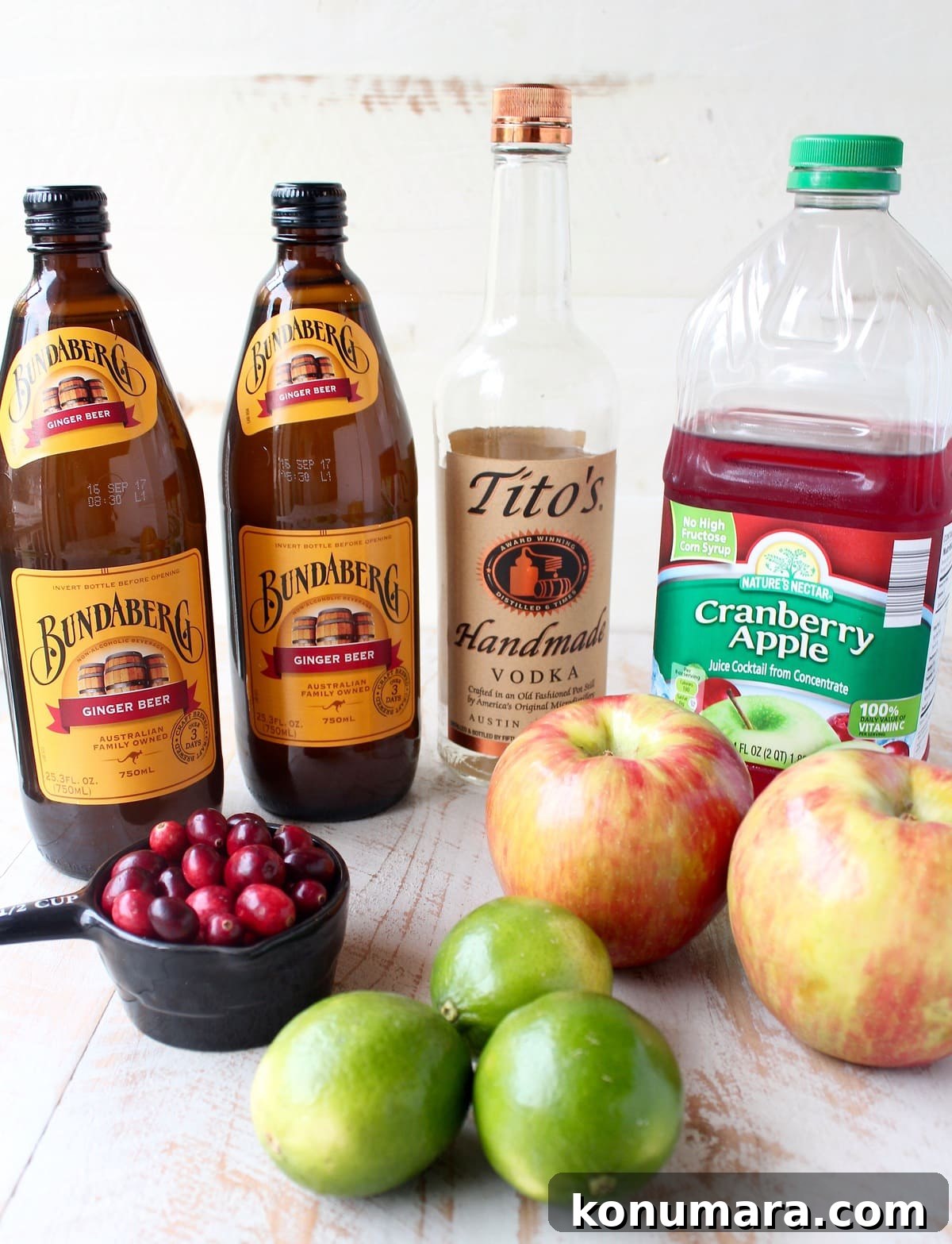 ingredients for cranberry apple moscow mule punch on a white wood board