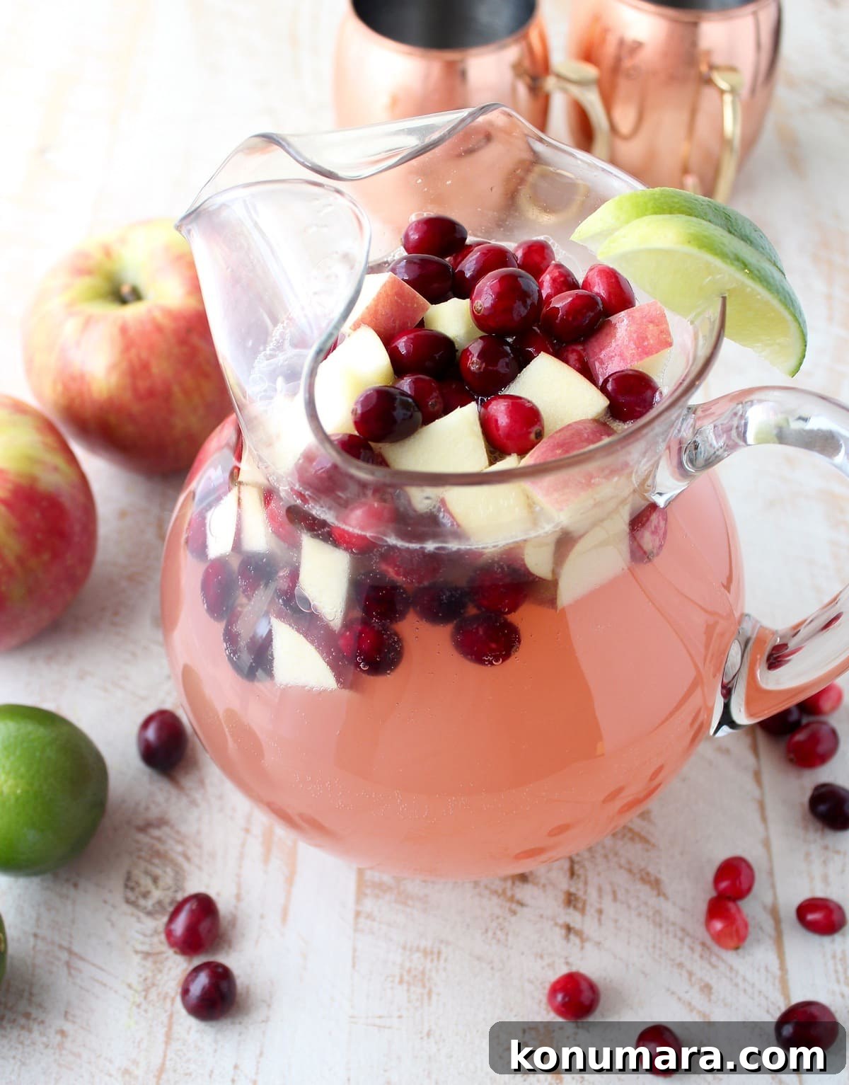 cranberry apple moscow mule punch in a large glass pitcher with fresh cranerries and diced apples