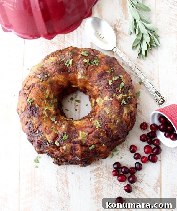 Savory Sausage Stuffing Recipe with Herbs 11 sausage stuffing baked in a bundt pan on a white wood board surrounded by fresh cranberries and rosemary