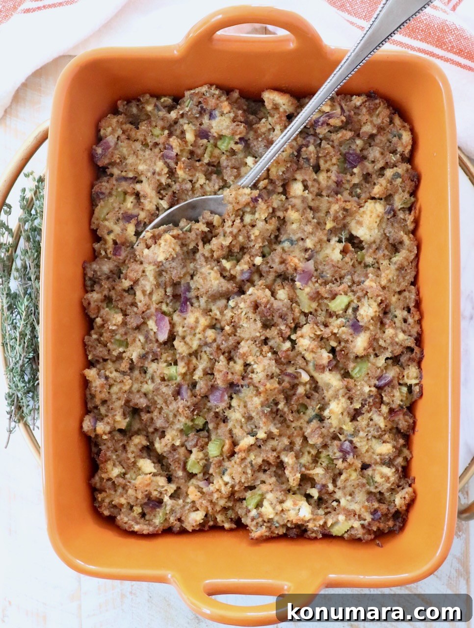 Savory Sausage Stuffing Recipe with Herbs 12 sausage stuffing in an orange casserole dish with a serving spoon