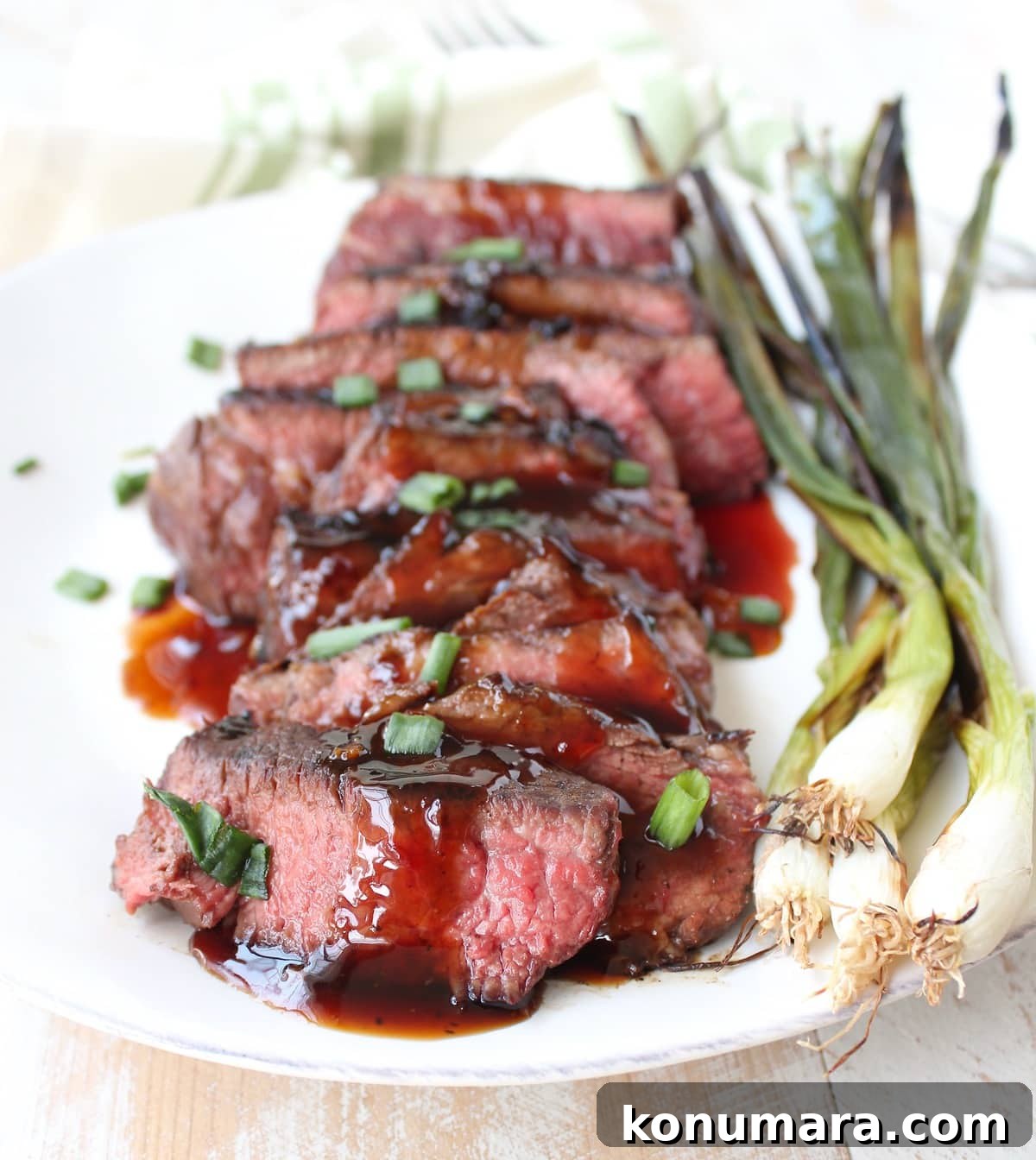 boneless beef short ribs sliced on a plate, drizzled with bbq sauce and topped with diced green onions with whole grilled green onions on the side