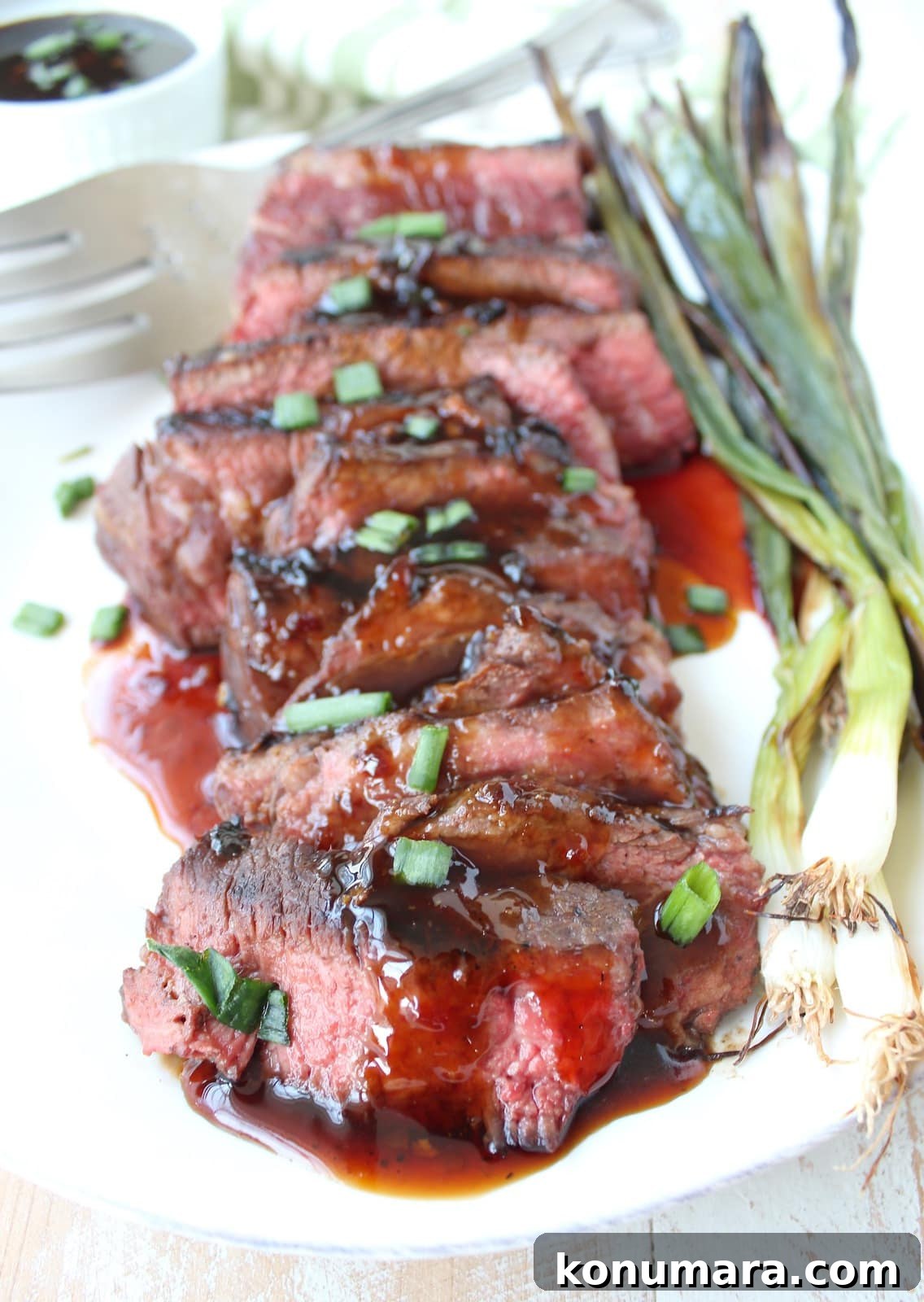 sliced cooked short ribs on a plate covered in Korean bbq sauce and diced green onions with grilled green onions on the side