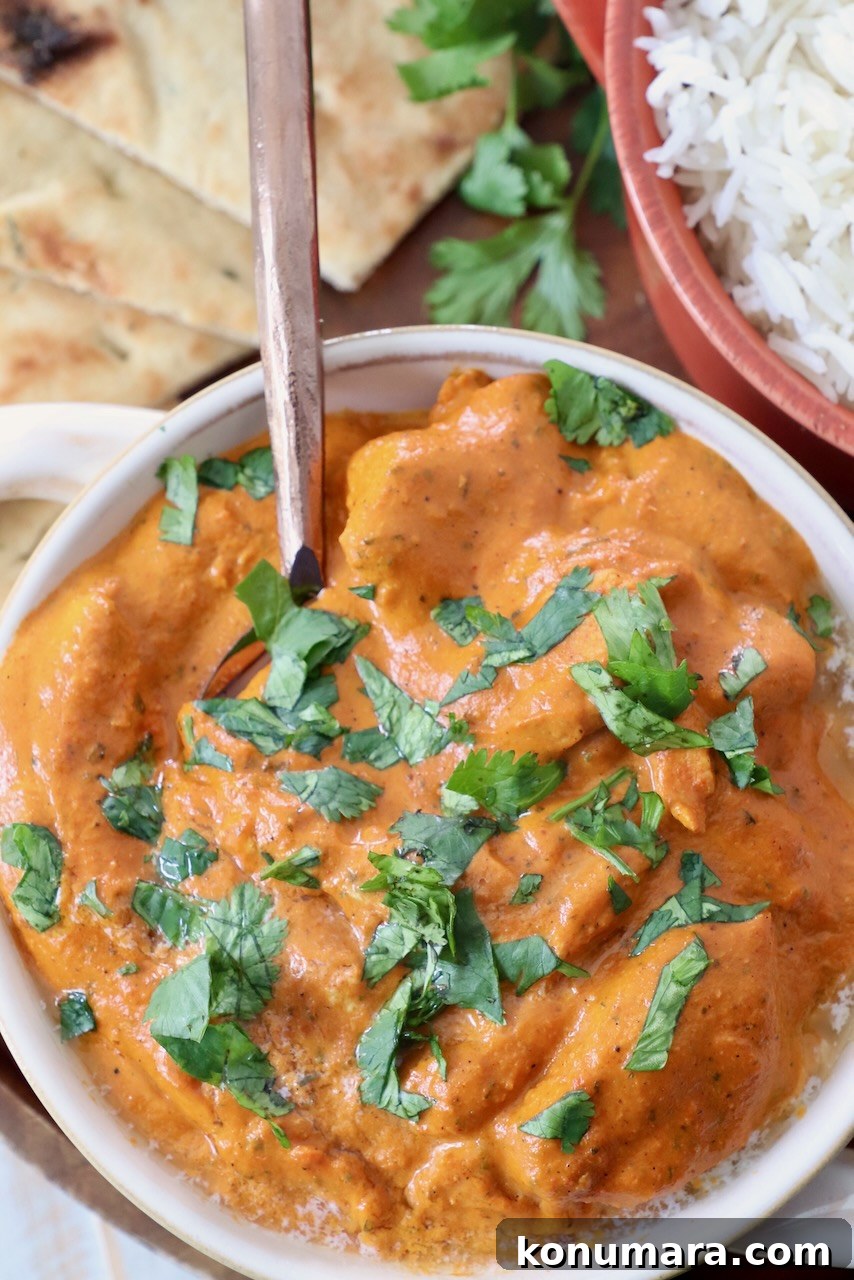 Authentic Indian Butter Chicken Recipe, Creamy and Rich 5 cooked chicken in butter curry sauce in bowl with spoon