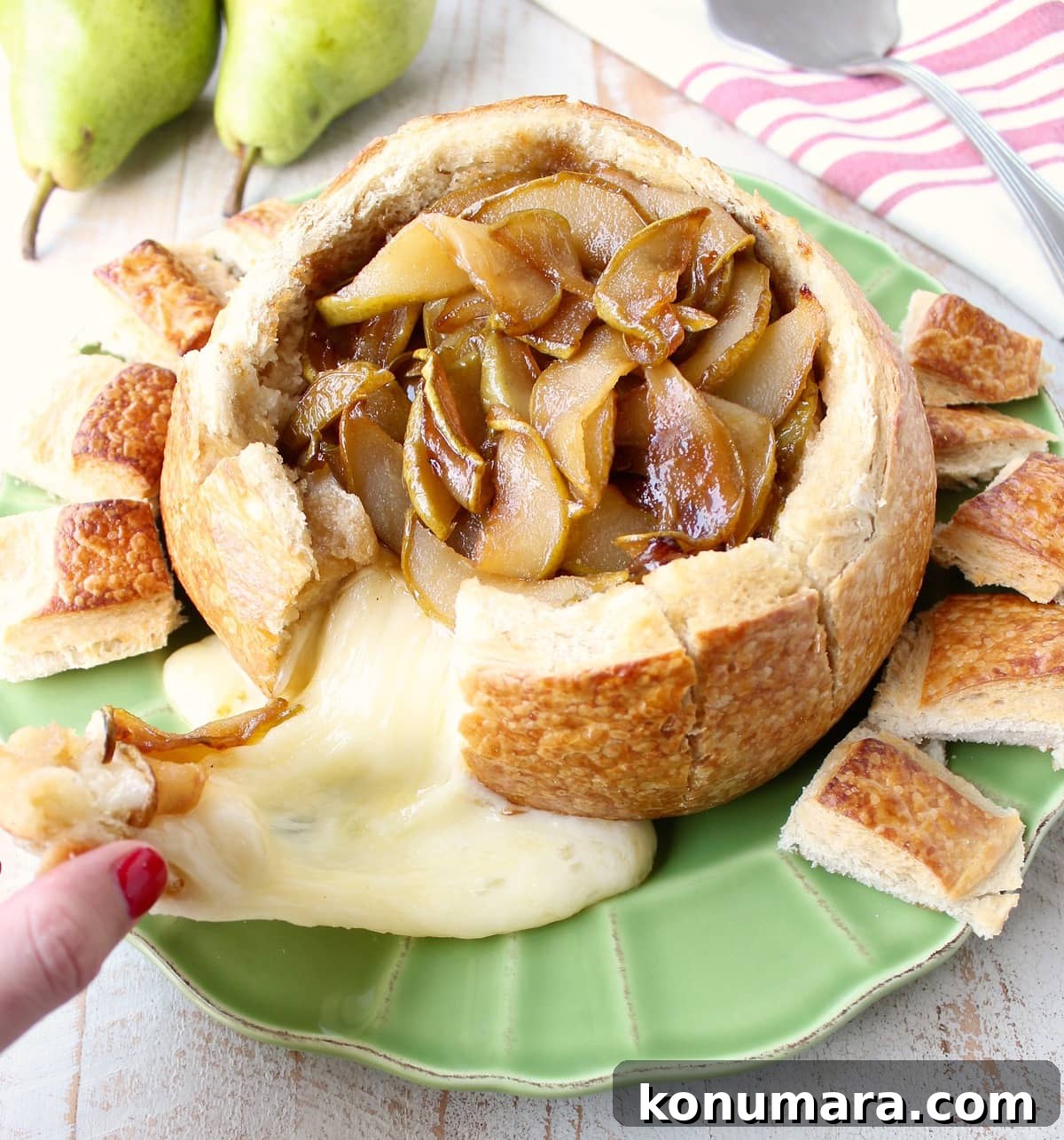 Brie cheese being pulled from a baked brie bread bowl with caramelized pears