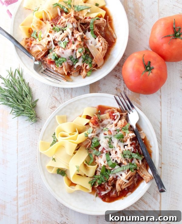 Slow Cooker Chicken Ragu Recipe with Tomatoes and Herbs 9 Two white plated topped with pasta, slow cooker chicken ragu, melted cheese, and fresh herbs all on a wooden surface.