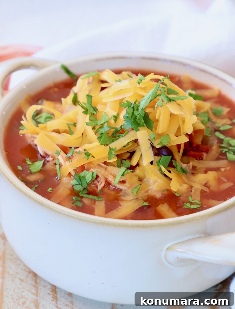 Creamy Slow Cooker Chicken Enchilada Soup 2 enchilada soup in white bowl topped with shredded cheddar cheese