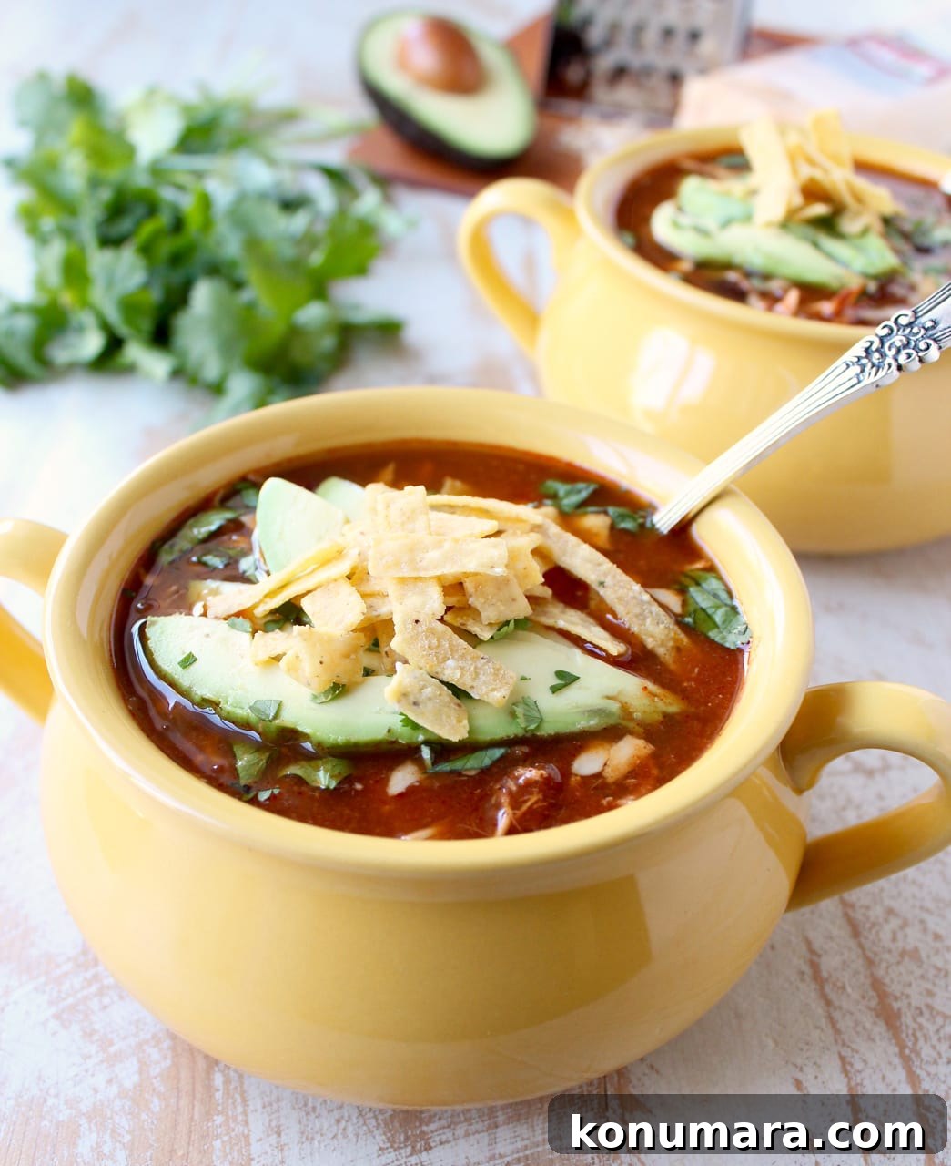Creamy Slow Cooker Chicken Enchilada Soup 7 A yellow bowl filled with enchilada soup topped with slices of avocado and tortilla strips with a second bowl in the background.