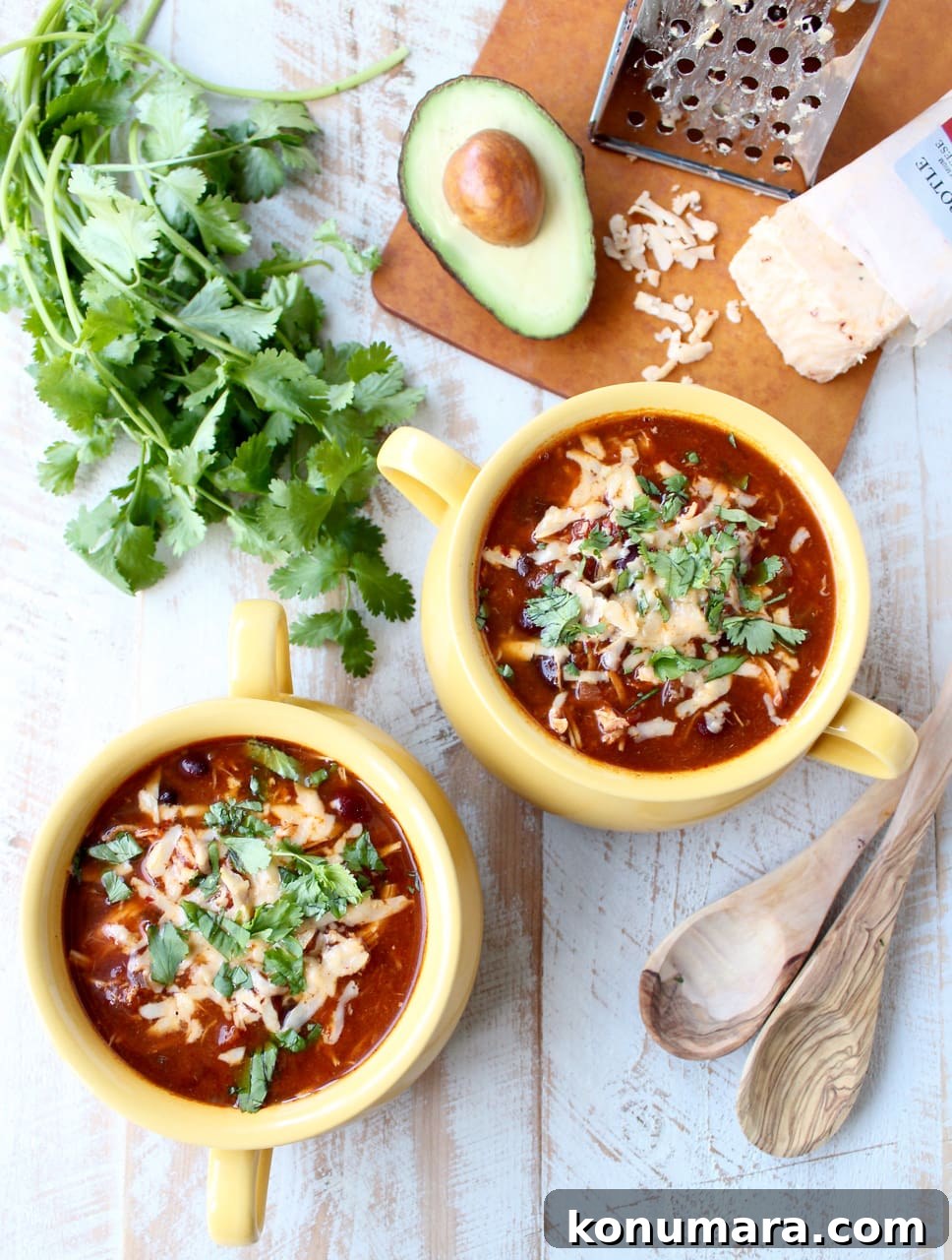 Creamy Slow Cooker Chicken Enchilada Soup 8 Two yellow bowls on a wooden surface filled with enchilada soup, cheese, and cilantro.