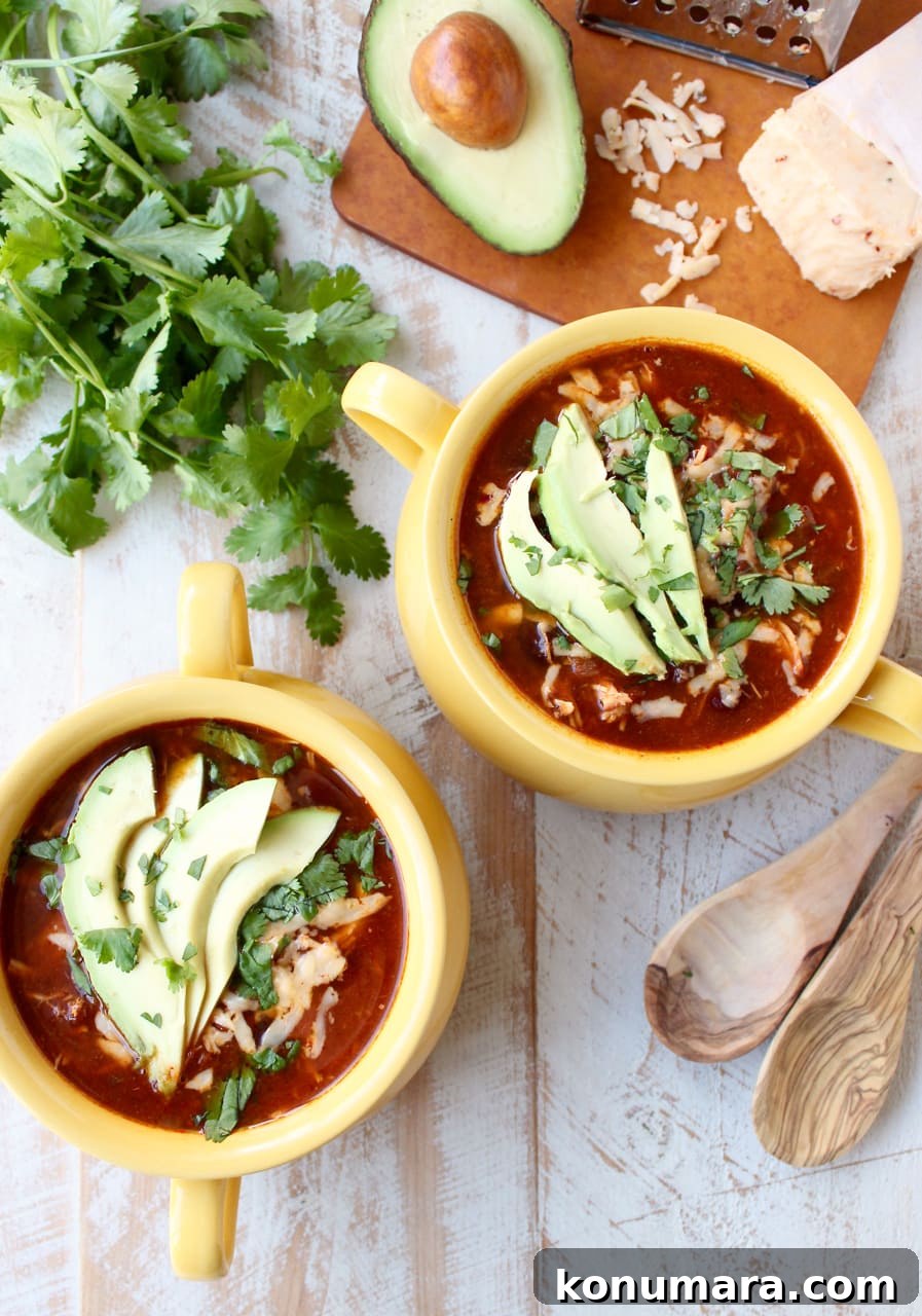 Creamy Slow Cooker Chicken Enchilada Soup 9 Top view of two yellow bowls filled with enchilada soup garnished with sliced avocado and cilantro.